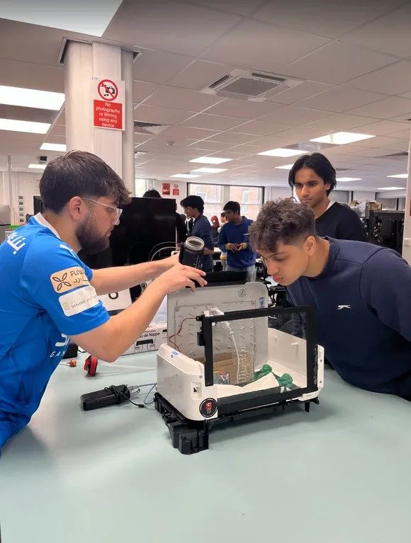 Two hackers lean over a gutted printer, rebuilding it into something new