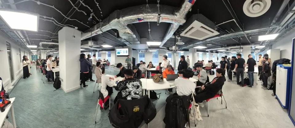 A packed workshop room, dozens of students building at round tables