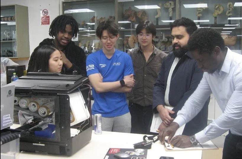 Judges and a team gather around a rebuilt printer during Hardware Hacks judging