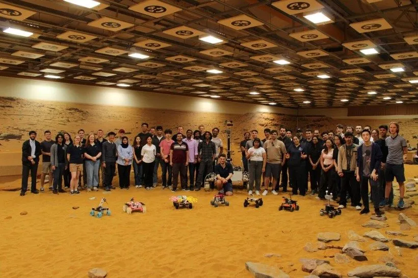 Competitors and a line of small rovers in a sand-filled Mars yard at the UKSEDS rover competition