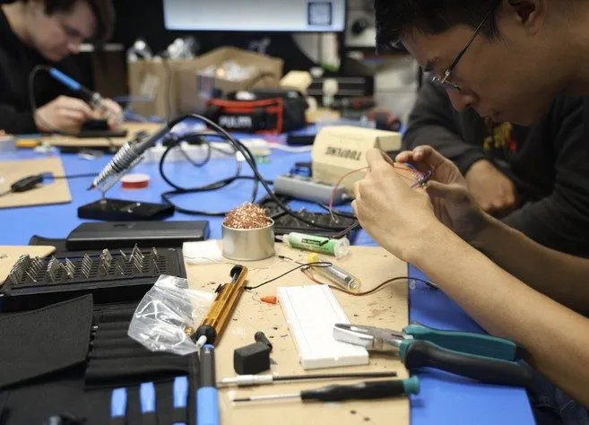 Students soldering at a bench covered in tools and components