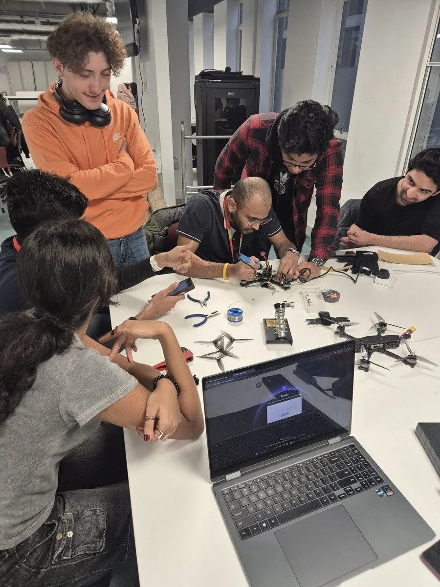 Members build and solder racing drones around a table