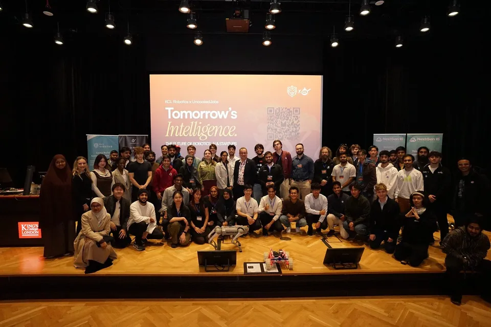 Dozens of attendees pose on stage in front of the Tomorrow’s Intelligence screen, with a robot dog at the front