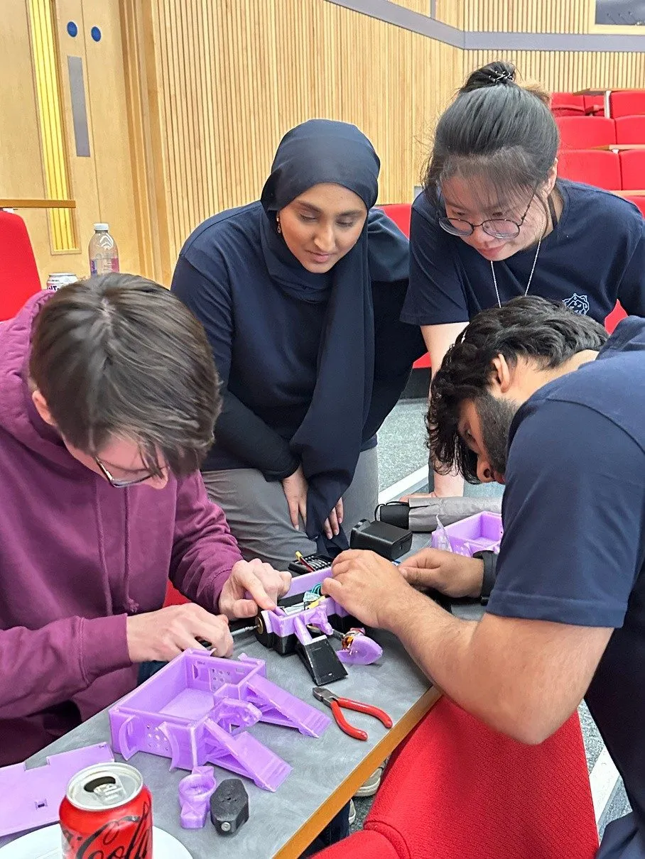 Four members repair a purple 3D-printed combat robot at RoboWars