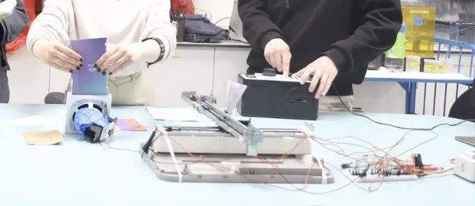 Hands test a home-made pen plotter built from printer rails